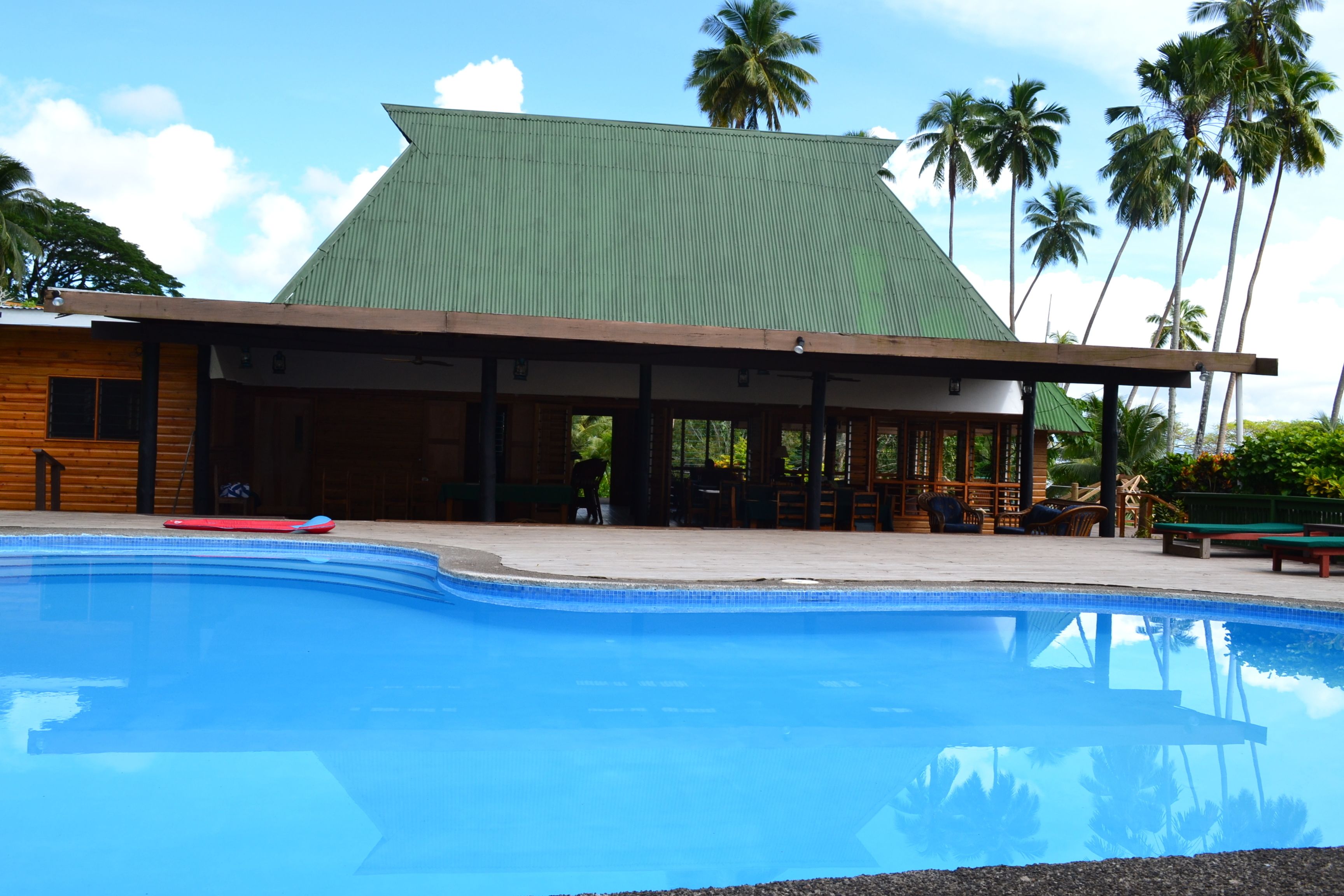Un espace aménagé au bord de la piscine, avec un bâtiment doté d’un toit végétalisé et d’une façade en bois.