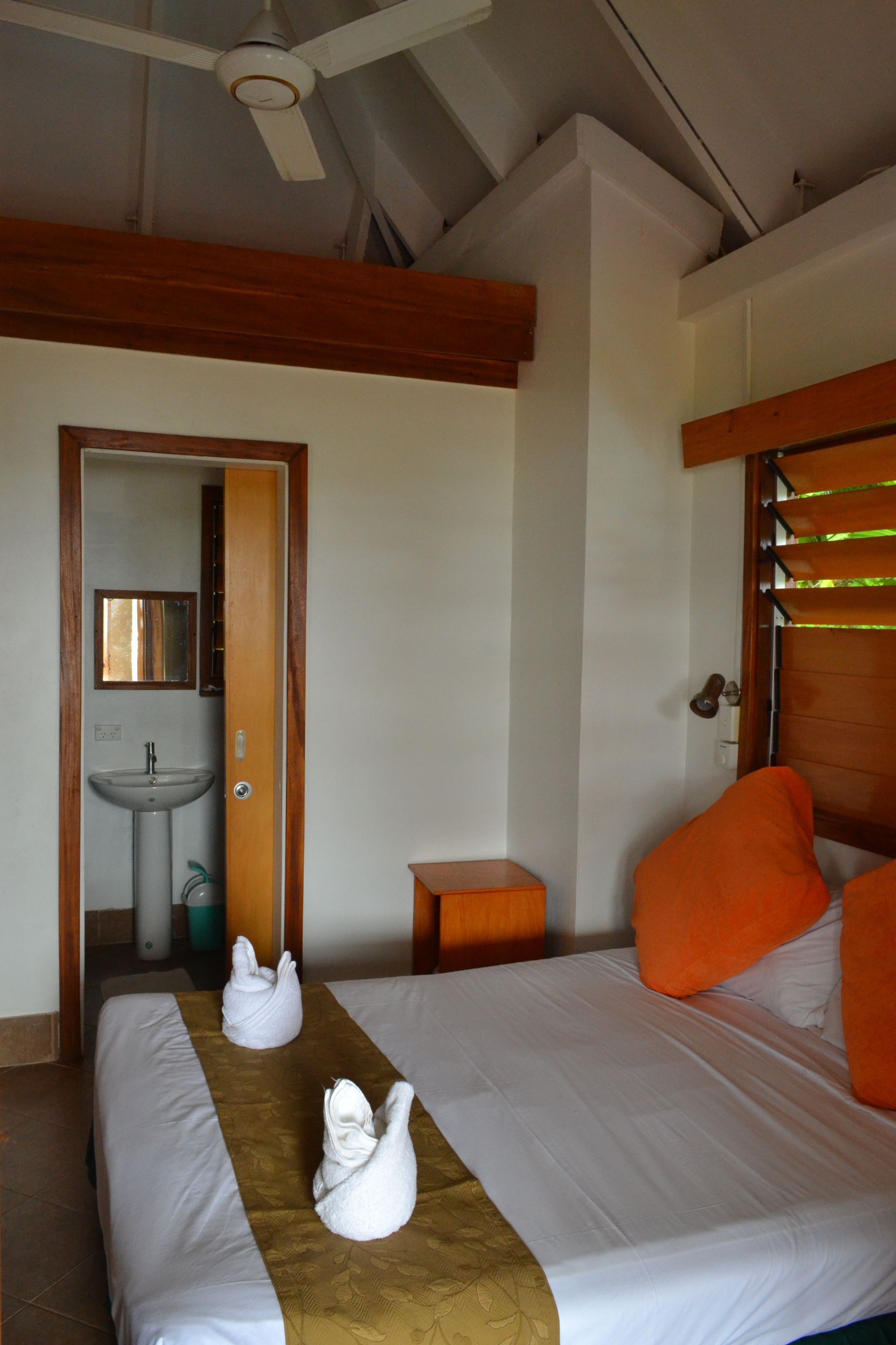 A hotel room with two beds, a small bathroom, and a ceiling fan.