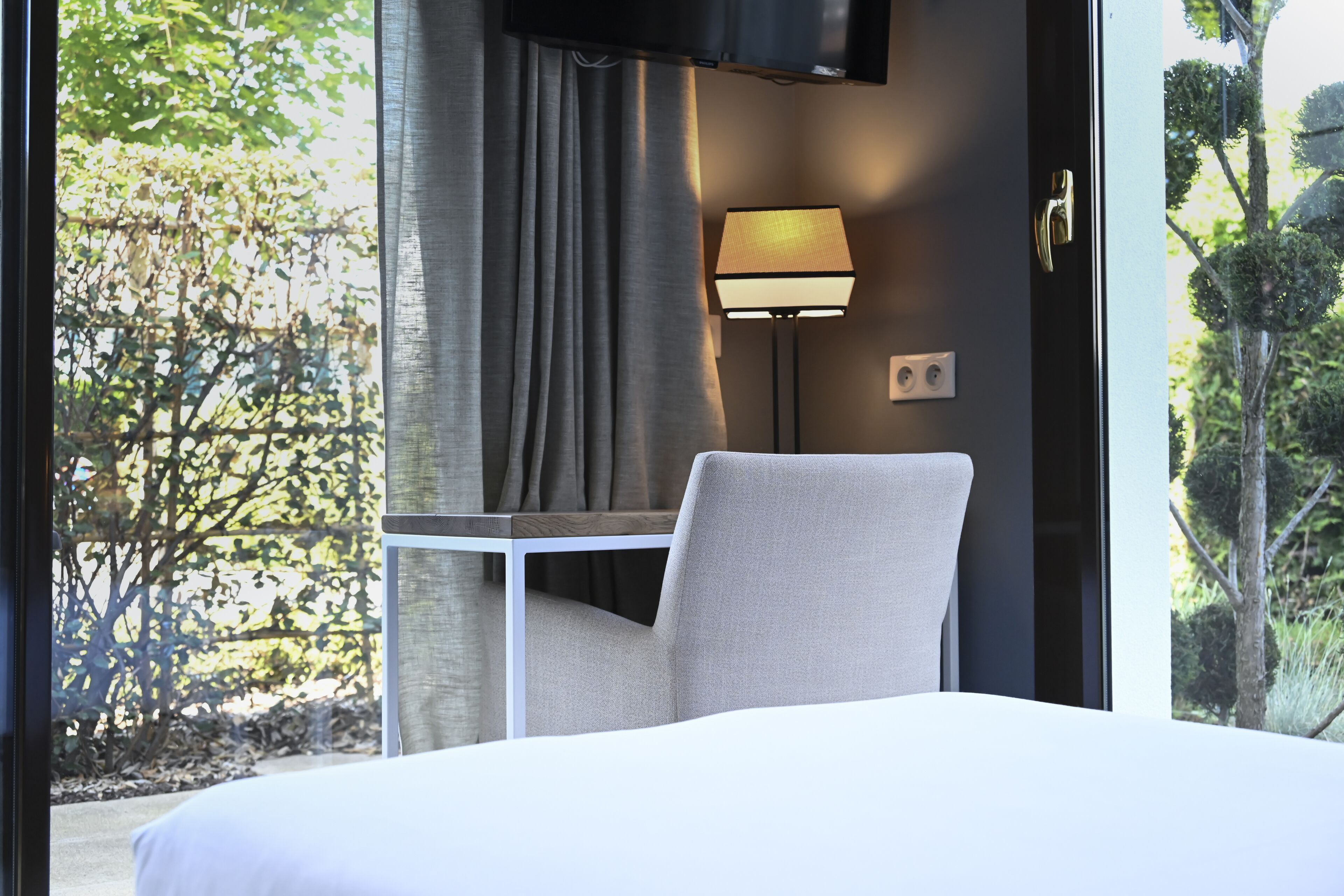 Una camera d'albergo con un letto, una sedia, un tavolo, una lampada e una televisione a parete.