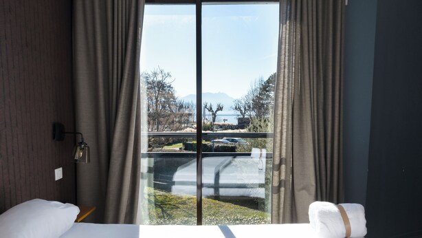 Een hotelkamer met een groot raam, een bed, een nachtkastje en een lamp.