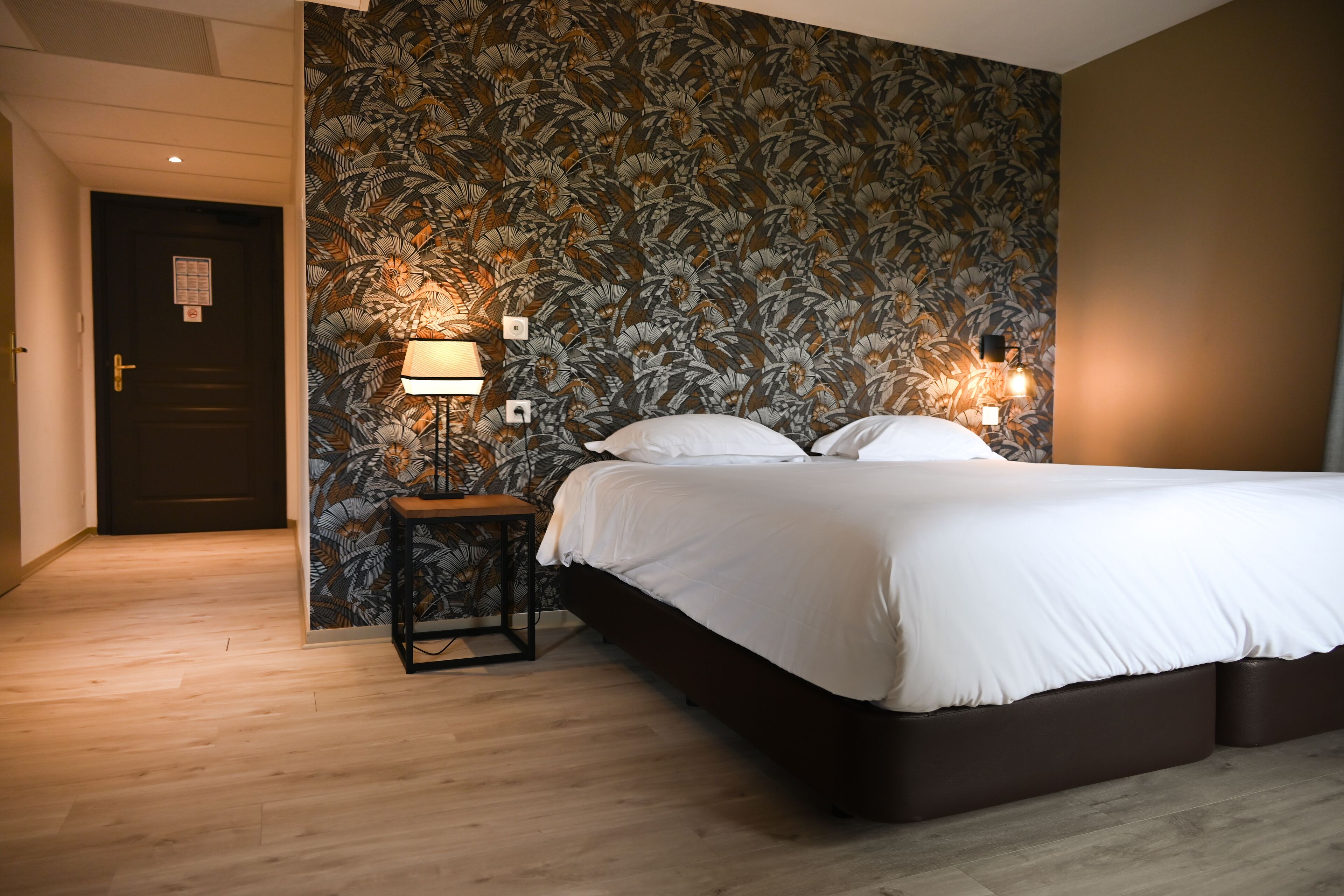 Un dormitorio con cama, mesita de noche, lámpara y pared con estampado floral.