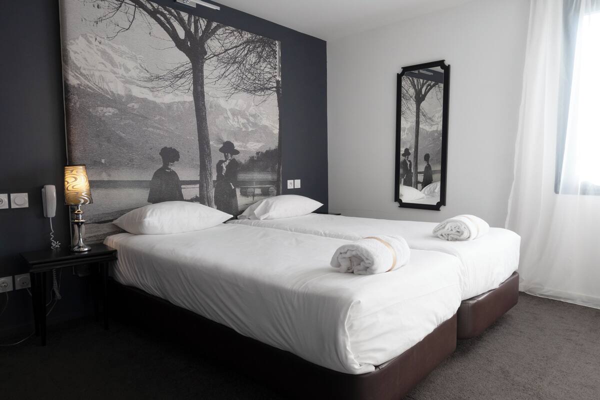 A hotel room with a large bed, a bedside lamp, a wall-mounted mirror, and a large painting.