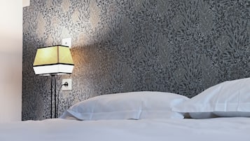 Een hotelkamer met behang met een patroon, een bedlampje en een opgemaakt bed met witte lakens.