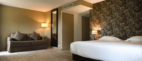 A hotel room with a sofa, a bed, a mirror, and a door leading to another room.