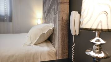 Ein ordentlich bezogenes Bett mit Kissen, einem fest montierten Telefon und einer Lampe mit marmorartigem Lampenschirm.