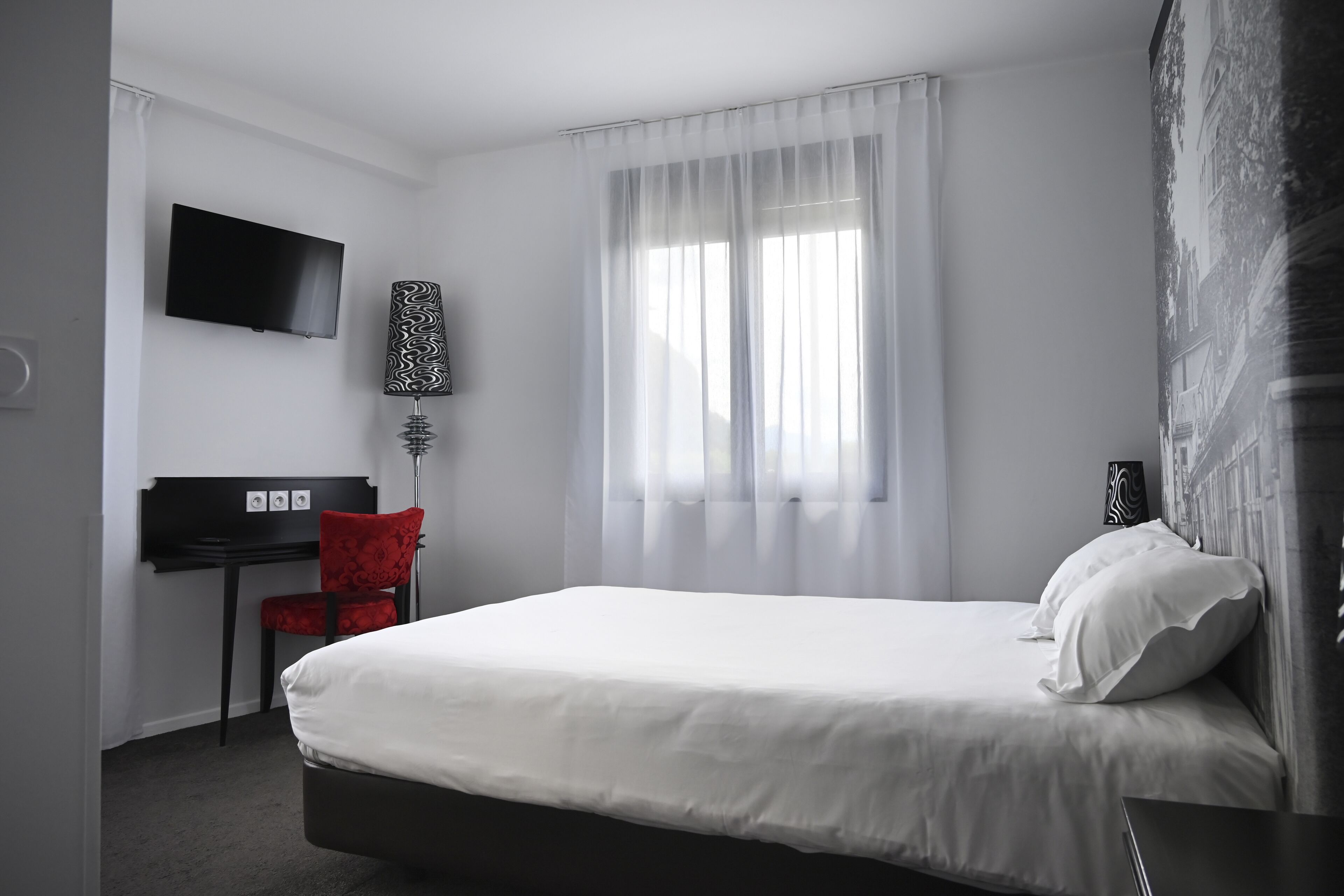 Habitació d'hotel amb llit, escriptori, cadira, televisió i finestra amb cortines.