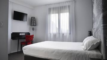 Ein Hotelzimmer mit Bett, Schreibtisch, Stuhl, Fernseher und einem Fenster mit Vorhängen.