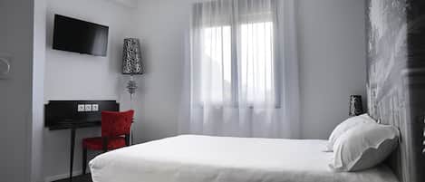 A hotel room with a bed, a desk, a chair, a TV, and a window with curtains.