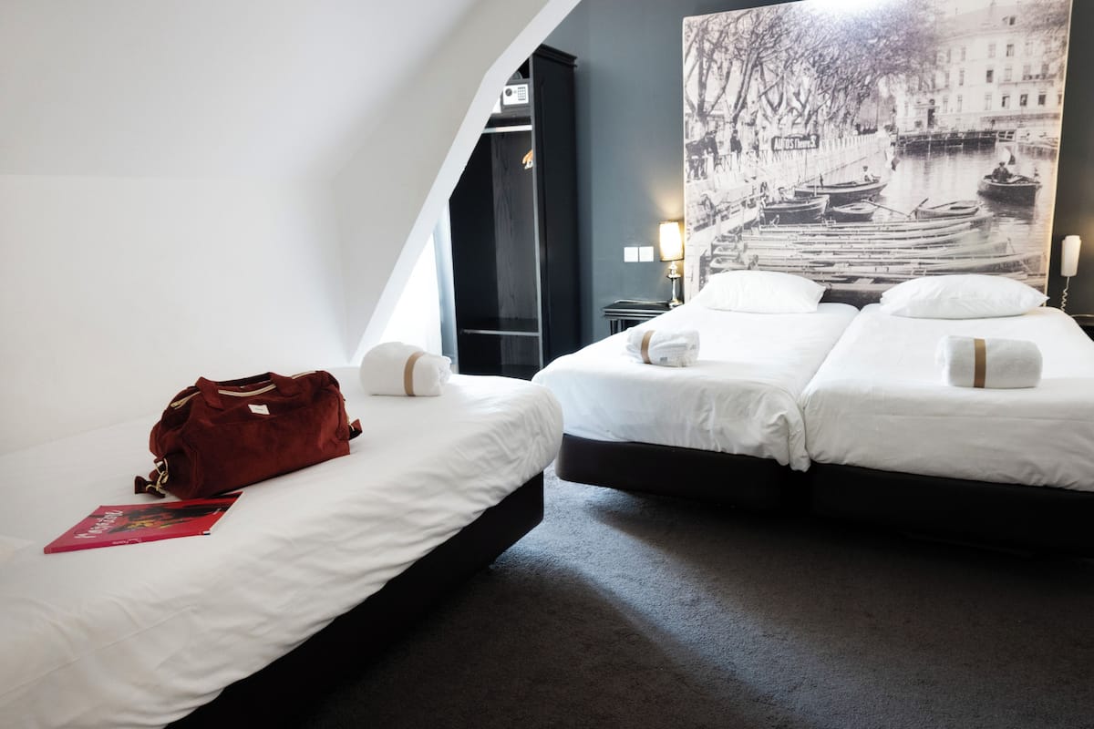 A hotel room with two beds, a red bag, and a wall-mounted lamp.