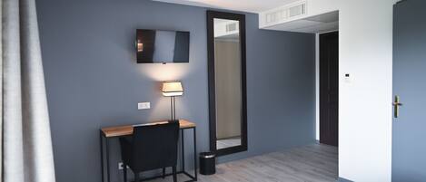 Una habitación de hotel con escritorio, silla, lámpara, espejo grande y una cama.
