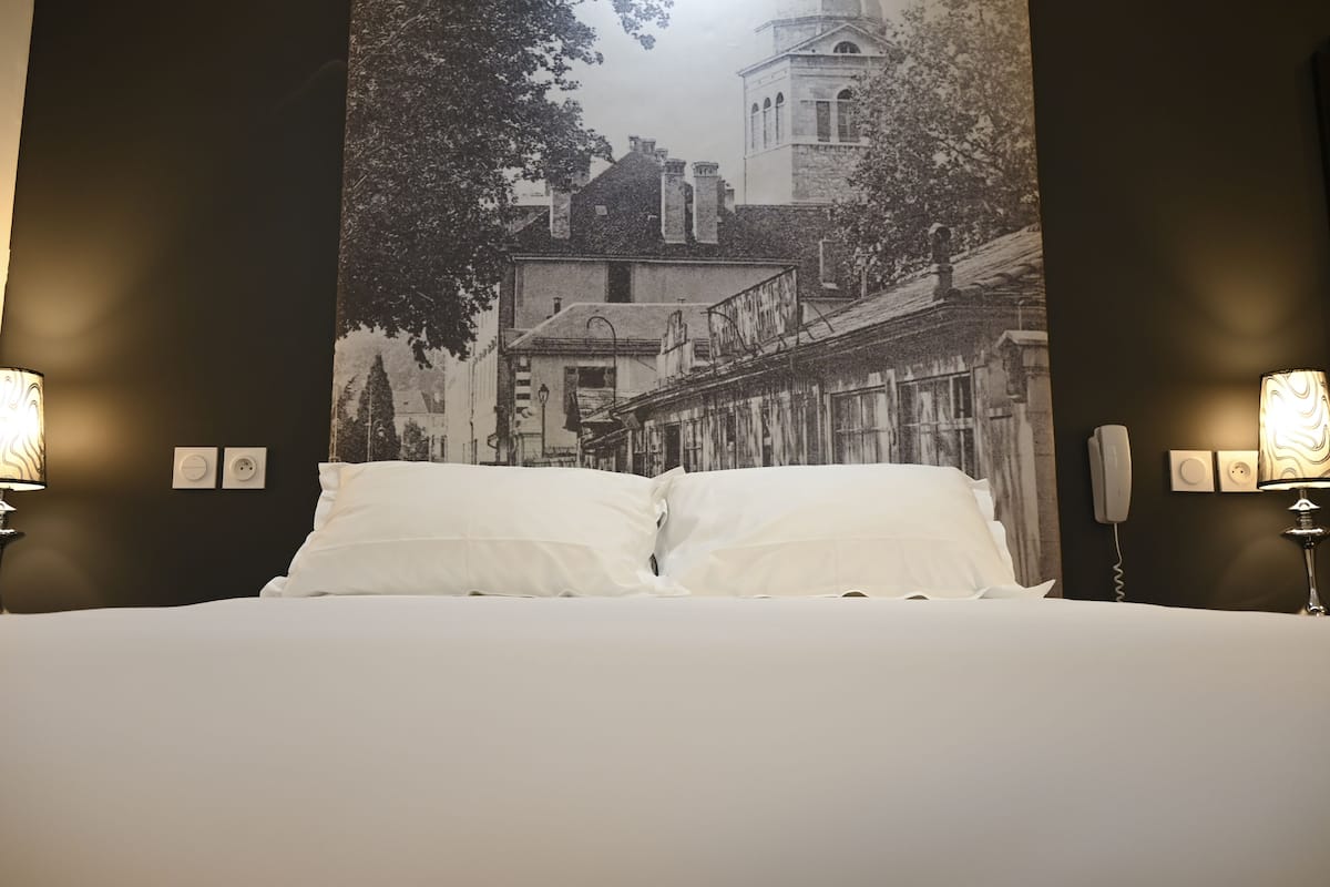 A hotel room with a large bed, two bedside lamps, and a wall tapestry depicting a cityscape.