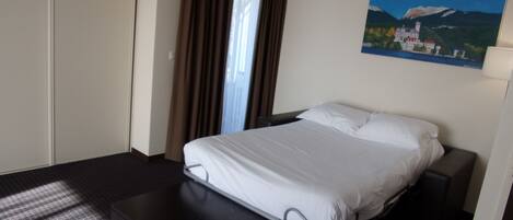 Ein Hotelzimmer mit Bett, Schreibtisch, einem Bild an der Wand und einem Fenster mit Vorhängen.