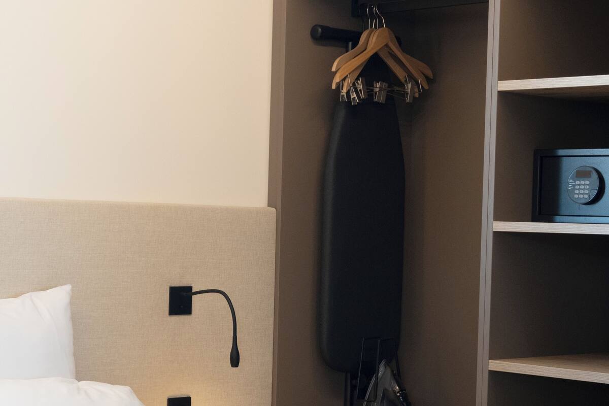 A hotel room with a bed, a nightstand with a lamp, a microwave, and a hanging clothes rack.
