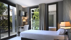 Een hotelkamer met een bed, een bureau, een stoel, een televisie en een balkon met gordijnen.