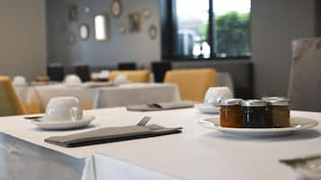 A dining table set with a white cup, saucer, cutlery, a napkin, and a plate with four condiment jars.
