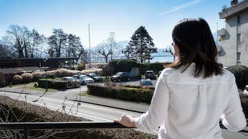 Mulher parada perto de um corrimão, com vista para um estacionamento com carros e um edifício ao fundo.