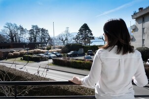 Mulher parada perto de um corrimão, com vista para um estacionamento com carros e um edifício ao fundo.