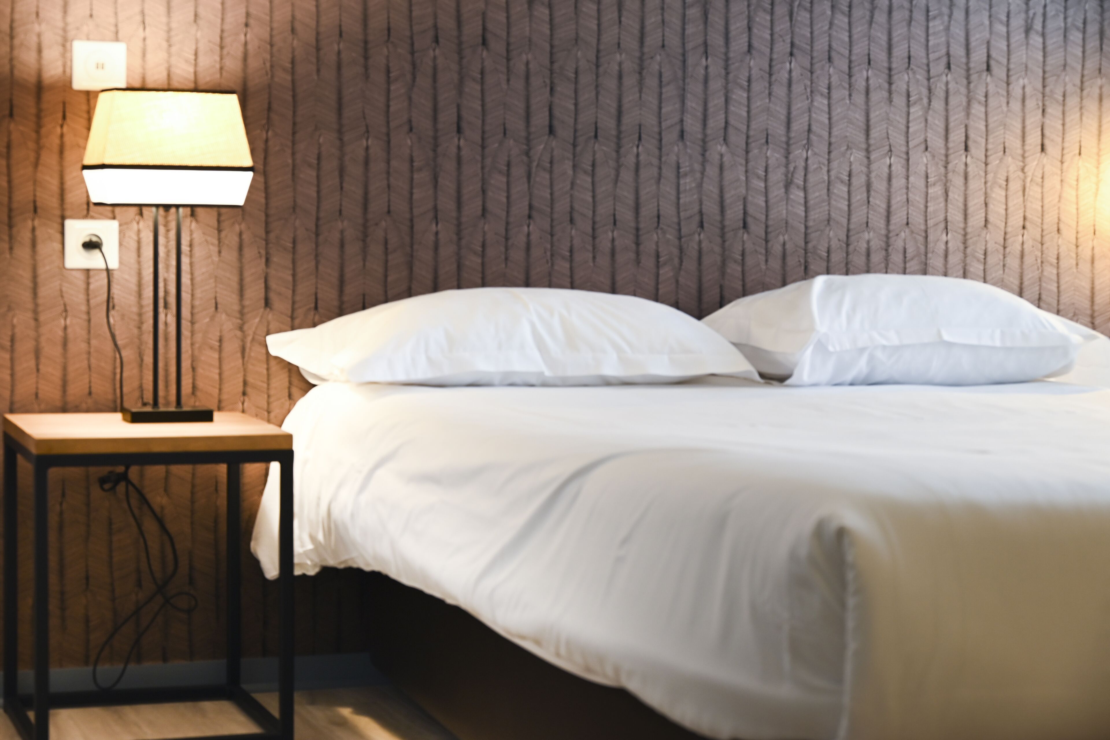 Ein ordentlich bezogenes Bett mit weißen Leinen in einem Zimmer mit Holzwandverkleidung.