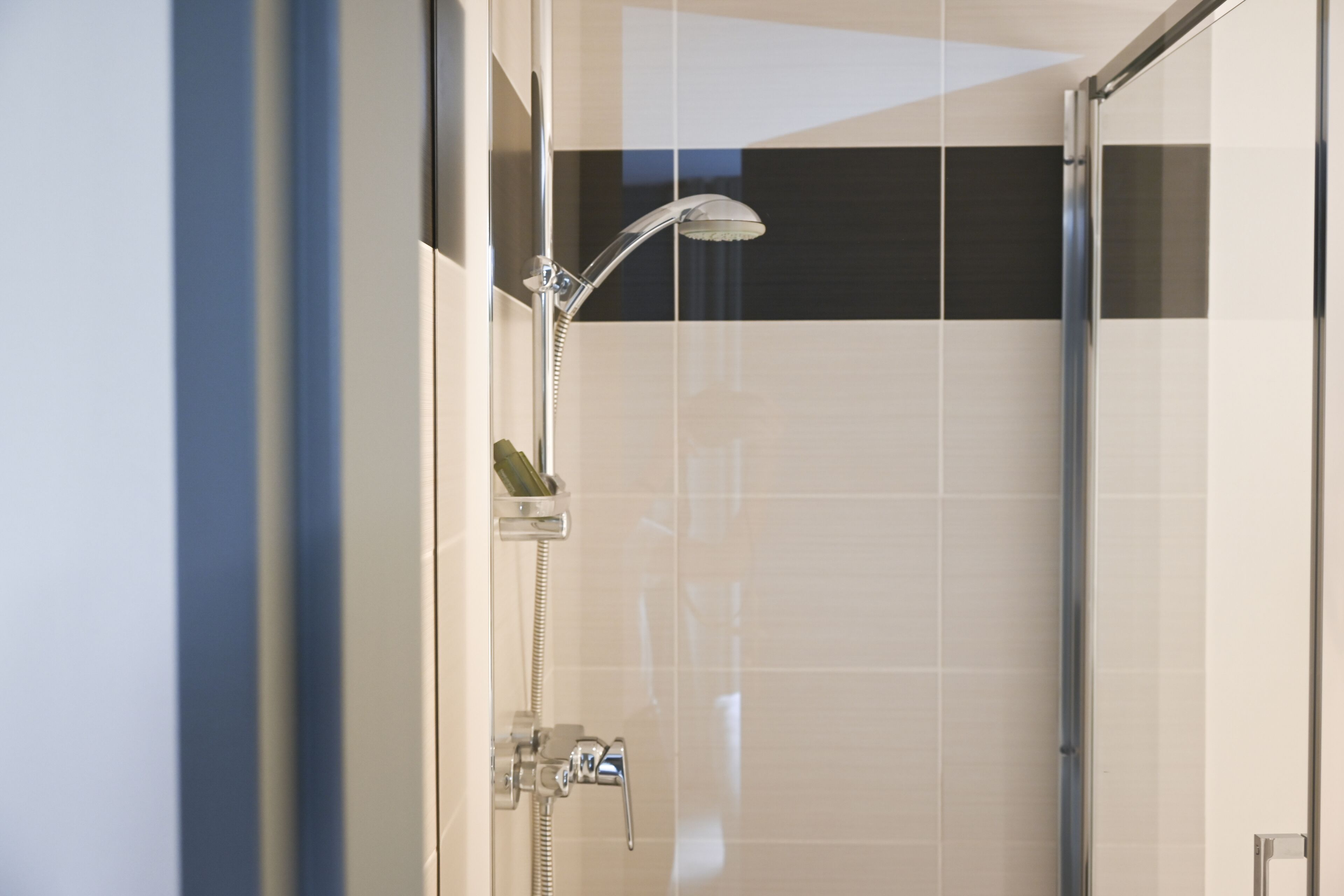 A modern bathroom with a glass shower enclosure, a handheld showerhead, and a wall-mounted faucet.