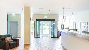A hotel lobby with a reception desk, a waiting area with a sofa, and a tiled floor. - Hotel Plöner See by Tulip Inn (Ploen)