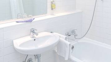 A bathroom with a white sink, a bathtub, and a mirror above the sink.