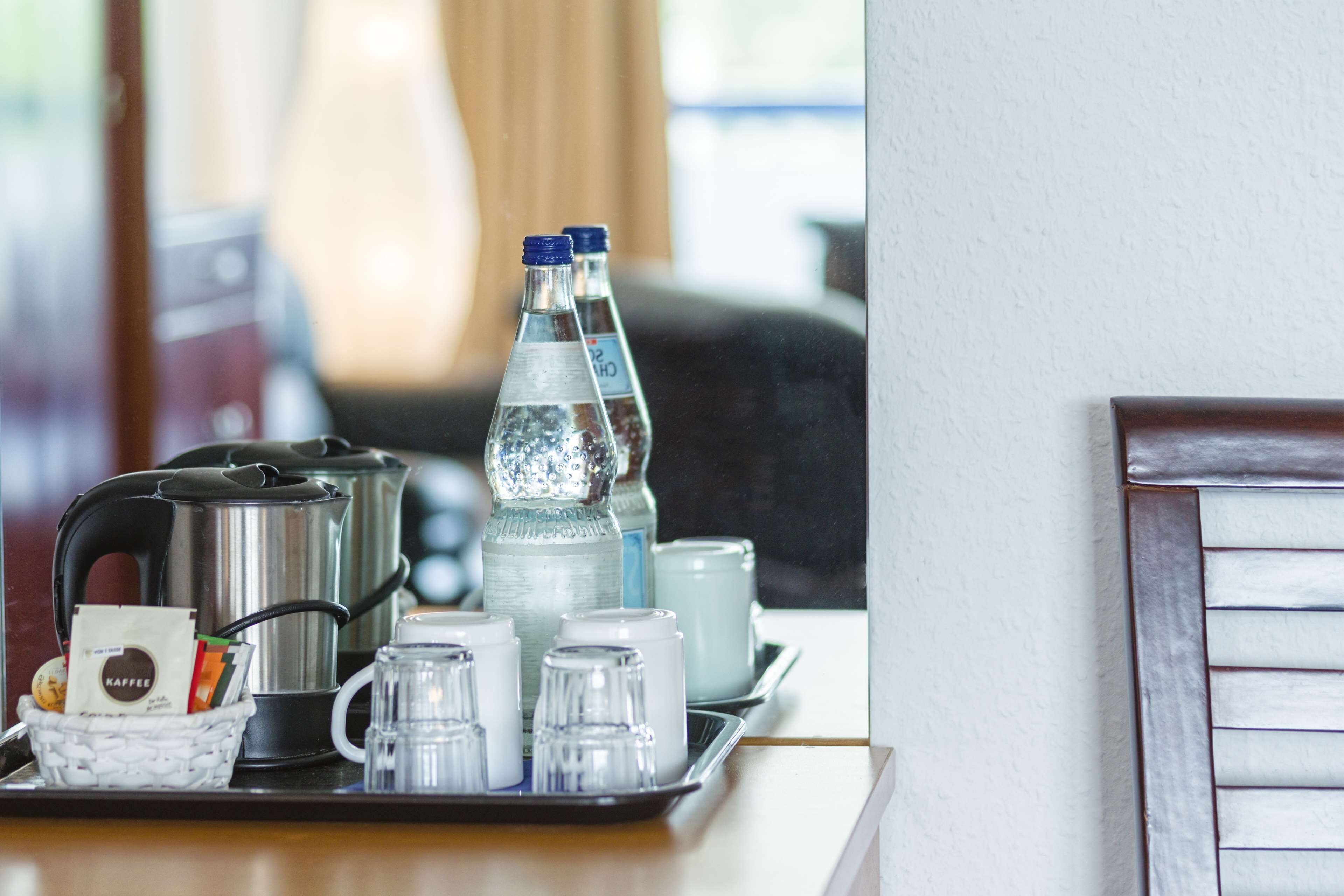 Una bandeja amb una cafetera, ampolles d'aigua i tasses de te sobre una taula d'hotel.