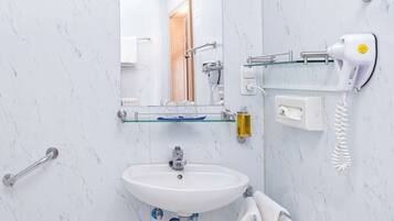 A bathroom with a white sink, a glass shelf, a hairdryer, and a mirror.