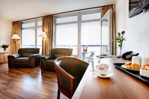 Relax in a spacious room with a comfortable seating area, large windows, and a minibar.