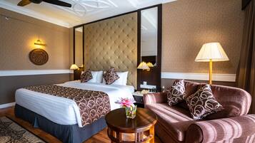 A hotel room with a large bed, a sofa, a small table, a lamp, and a ceiling fan.
