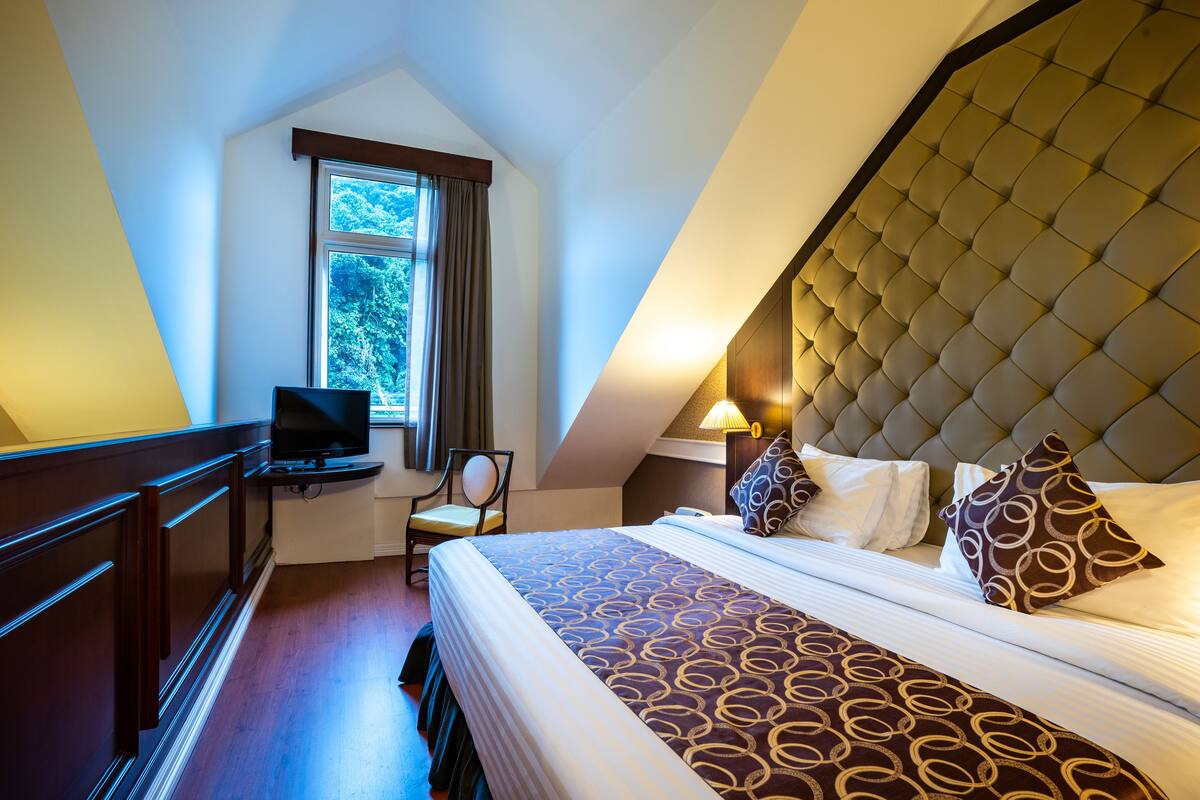 Una habitación de hotel con una cama grande, televisión, escritorio y ventana con cortinas.