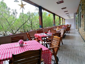 A restaurant with outdoor seating, red and white checkered tablecloths, wooden chairs, and star decorations on the ceiling.