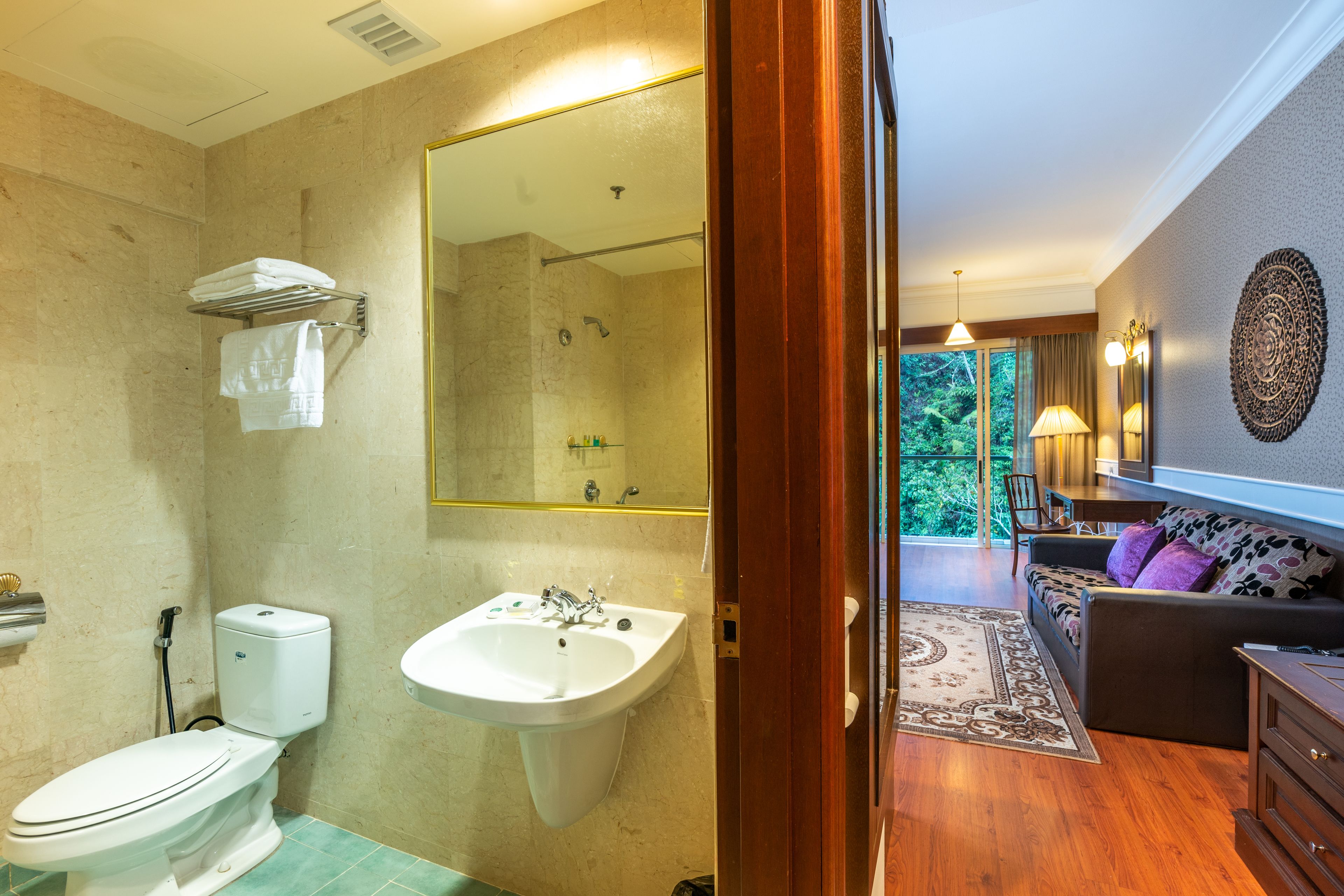 A bathroom with a toilet, sink, and shower. There is a mirror above the sink and a towel rack. The bathroom has beige walls and a wooden floor.