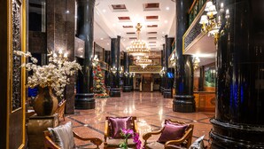 A spacious lobby with marble flooring, ornate columns, and a grand chandelier.