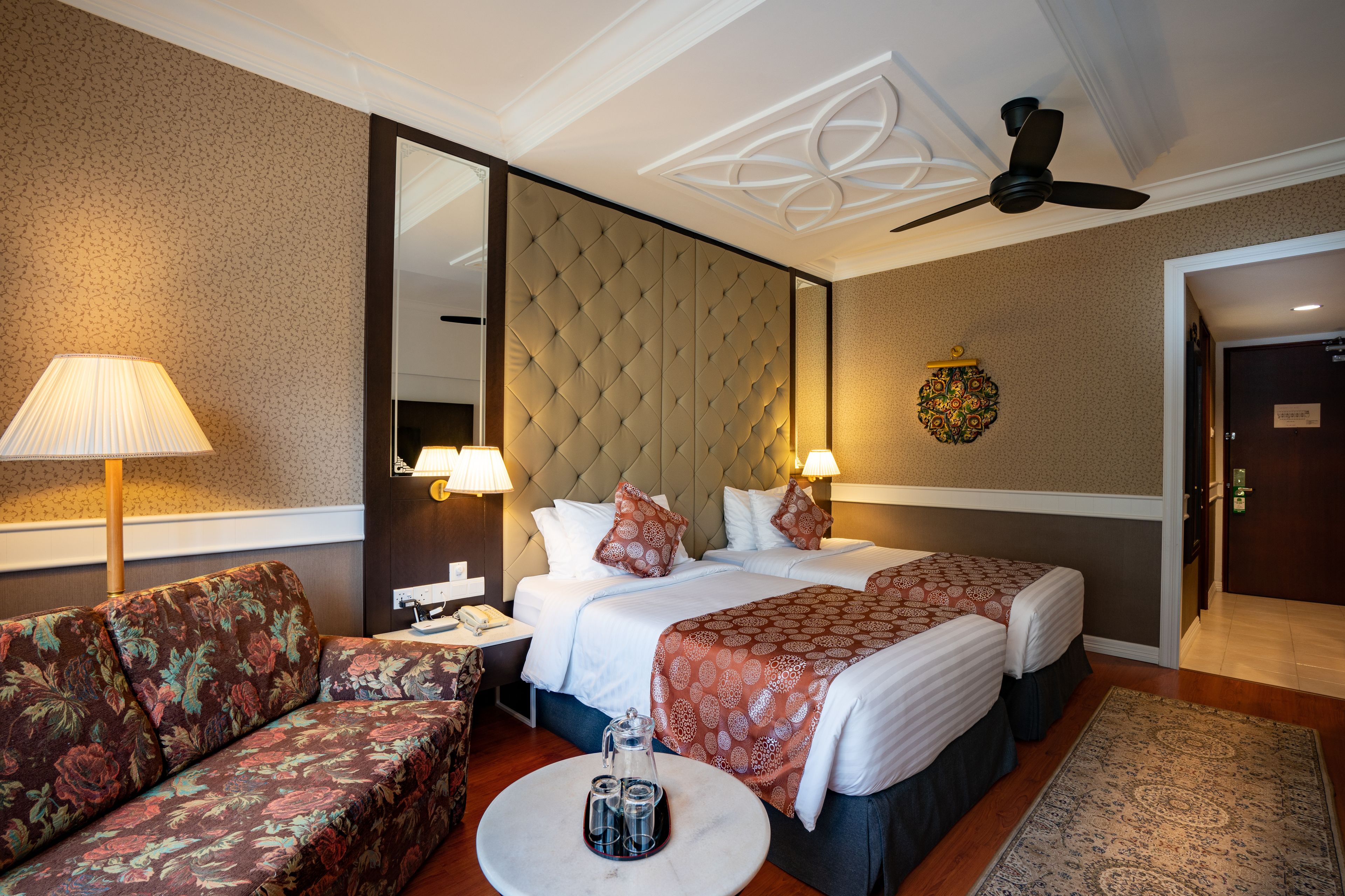A hotel room with two beds, a sofa, a coffee table, and a ceiling fan.