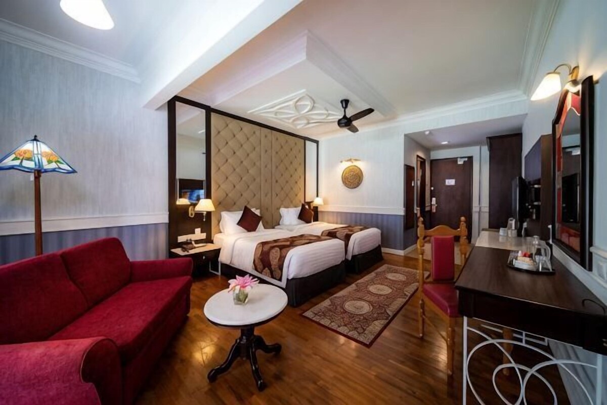 A hotel room with a bed, a red sofa, a small table, a mirror, and a ceiling fan.