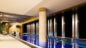 A modern indoor swimming pool with a central column, glass walls, and a clean, reflective floor.