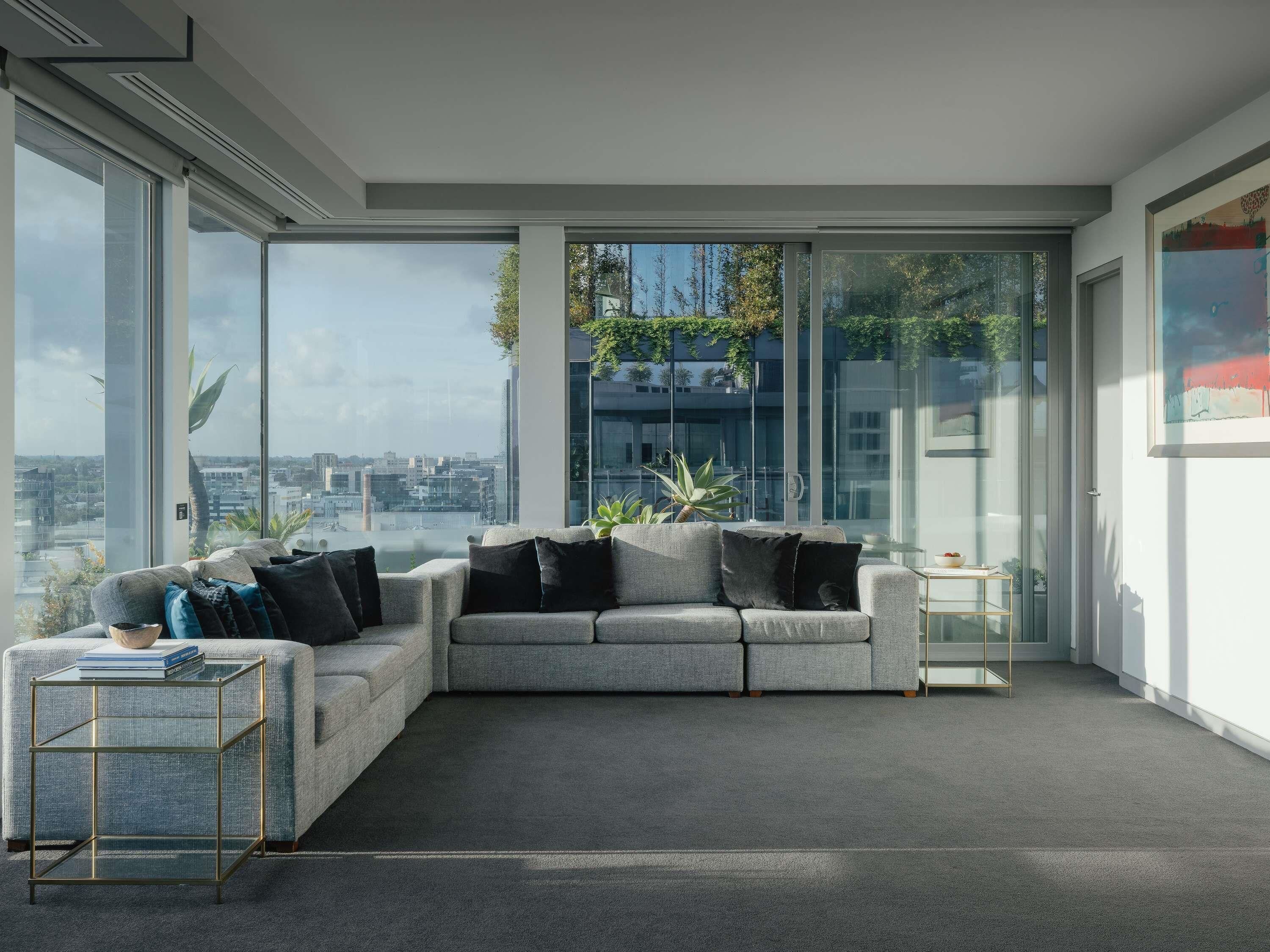 Una sala de estar moderna con un sofá gris, cojines negros y una mesa de centro de vidrio.