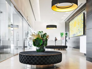 A modern lobby with glass walls, a round black seating area with a plant, and a large abstract painting on the wall. - The Olsen Melbourne - Art Series (South Yarra)