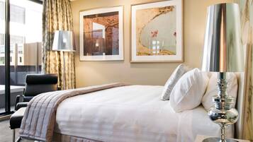 A hotel room with a bed, a chair, a lamp, and two framed artworks on the wall.