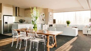 Una cocina moderna con horno empotrado, un comedor con mesa de madera y sillas transparentes, y una sala de estar con sofá y un ventanal grande.