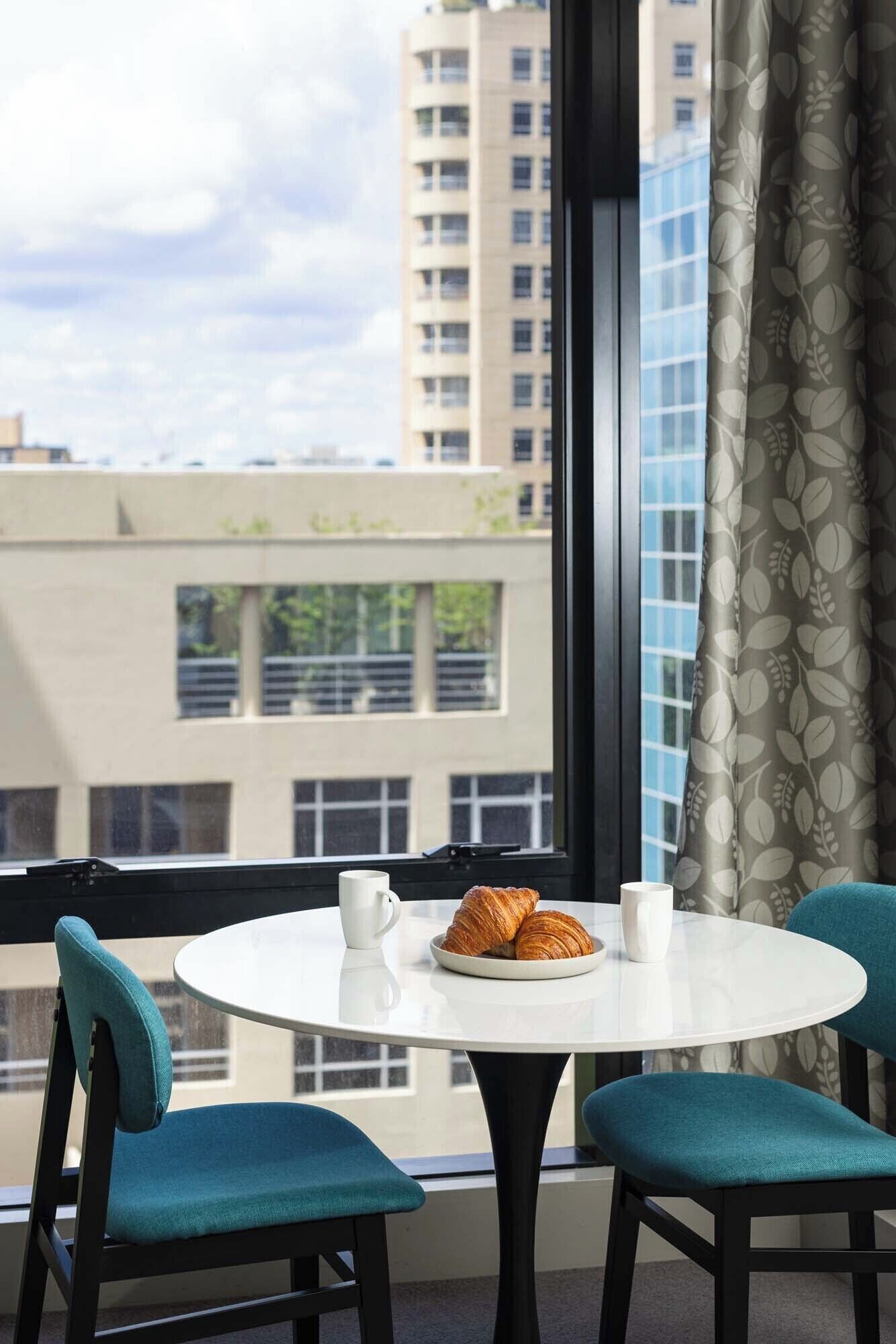 A round table with two chairs, a plate of croissants, and two white mugs.