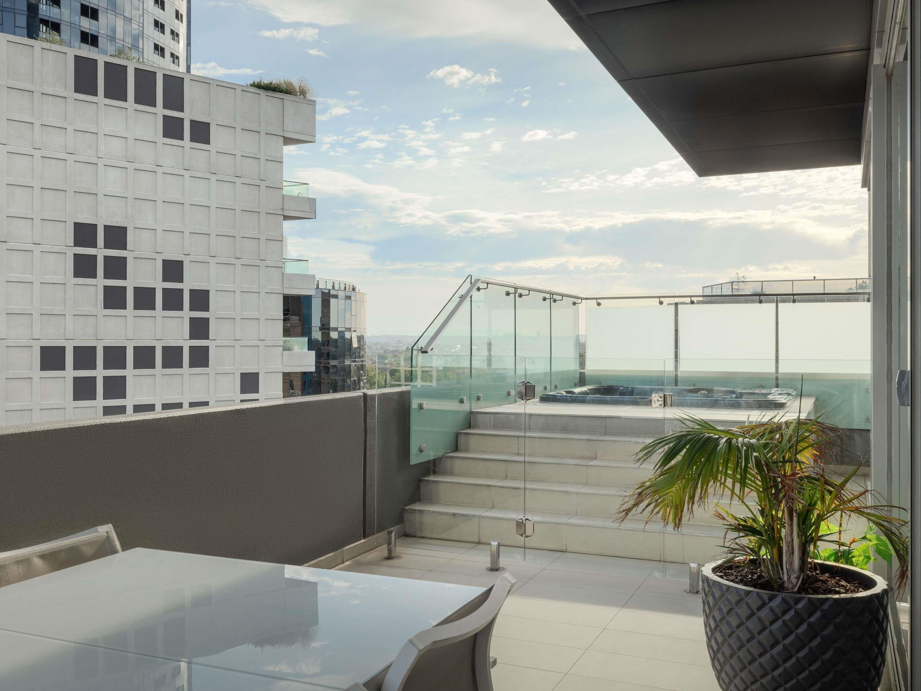 A rooftop terrace with a glass balustrade, a seating area, and a potted plant.