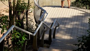 A wooden deck with metal railings overlooking a calm body of water and a sandy beach. - RACV Noosa Resort (Noosa Heads)
