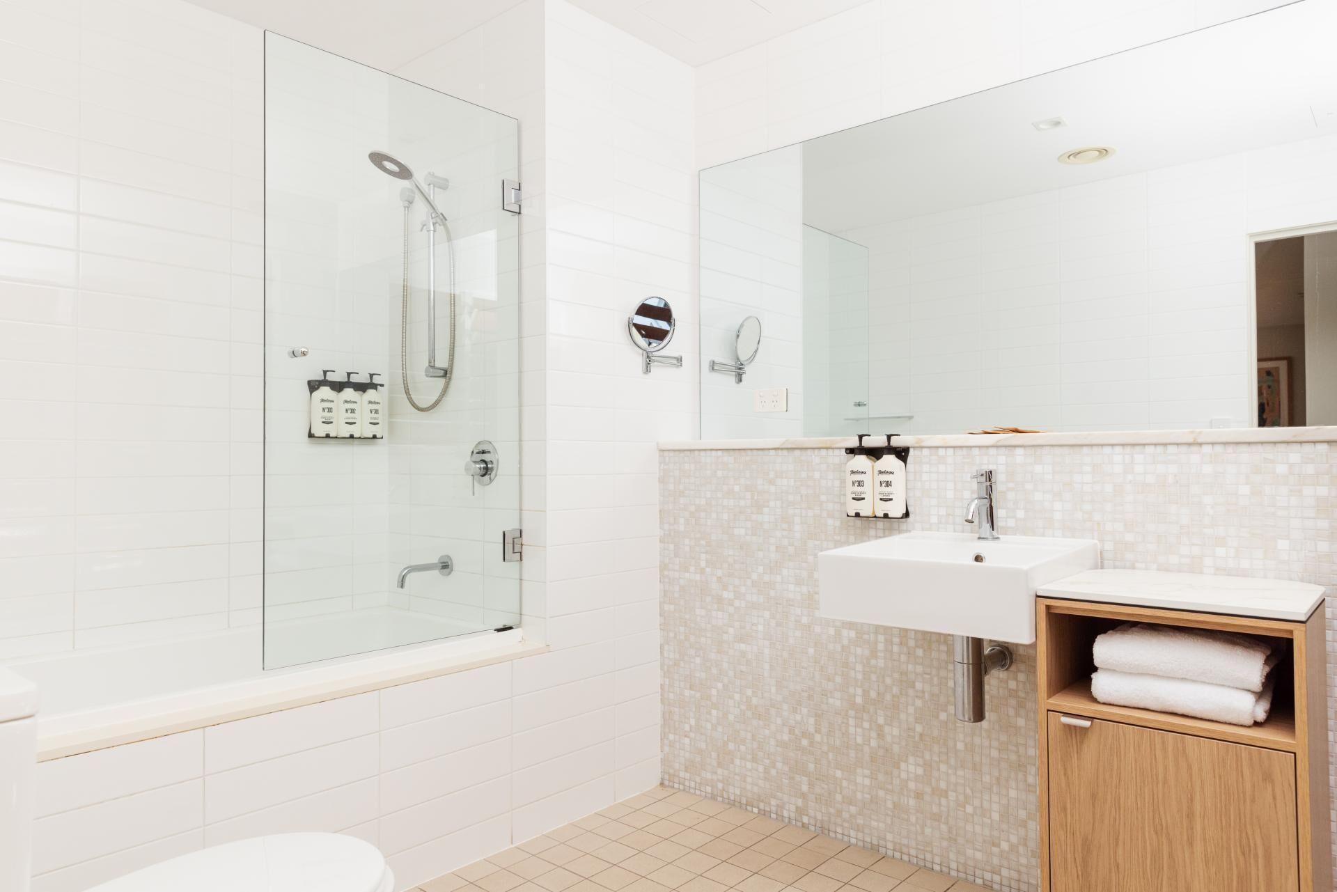 A modern bathroom with a glass-enclosed shower, a large mirror, a sink with a towel rack, and a toilet.