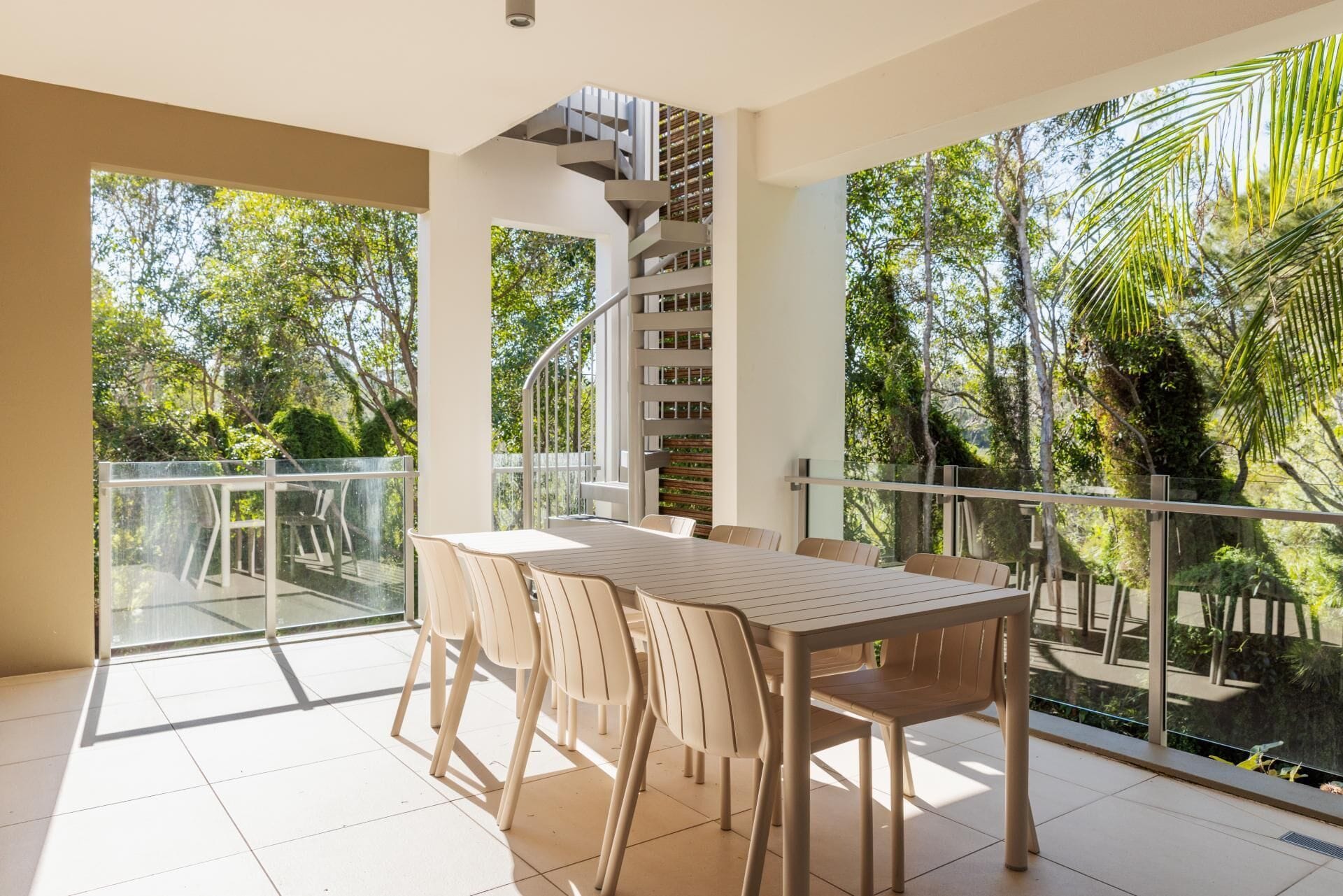 A balcony with a table and chairs, a spiral staircase, and a view of greenery.