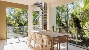 A balcony with a table and chairs, a spiral staircase, and a view of greenery.