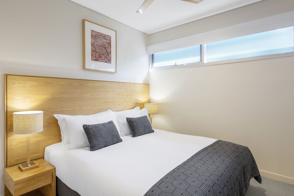 A hotel room with a bed, a nightstand, a lamp, a framed picture on the wall, and a window.