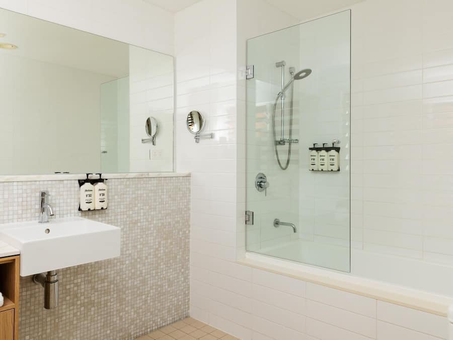 A bathroom with a white sink, a large mirror, a glass-enclosed shower, and a tiled backsplash.