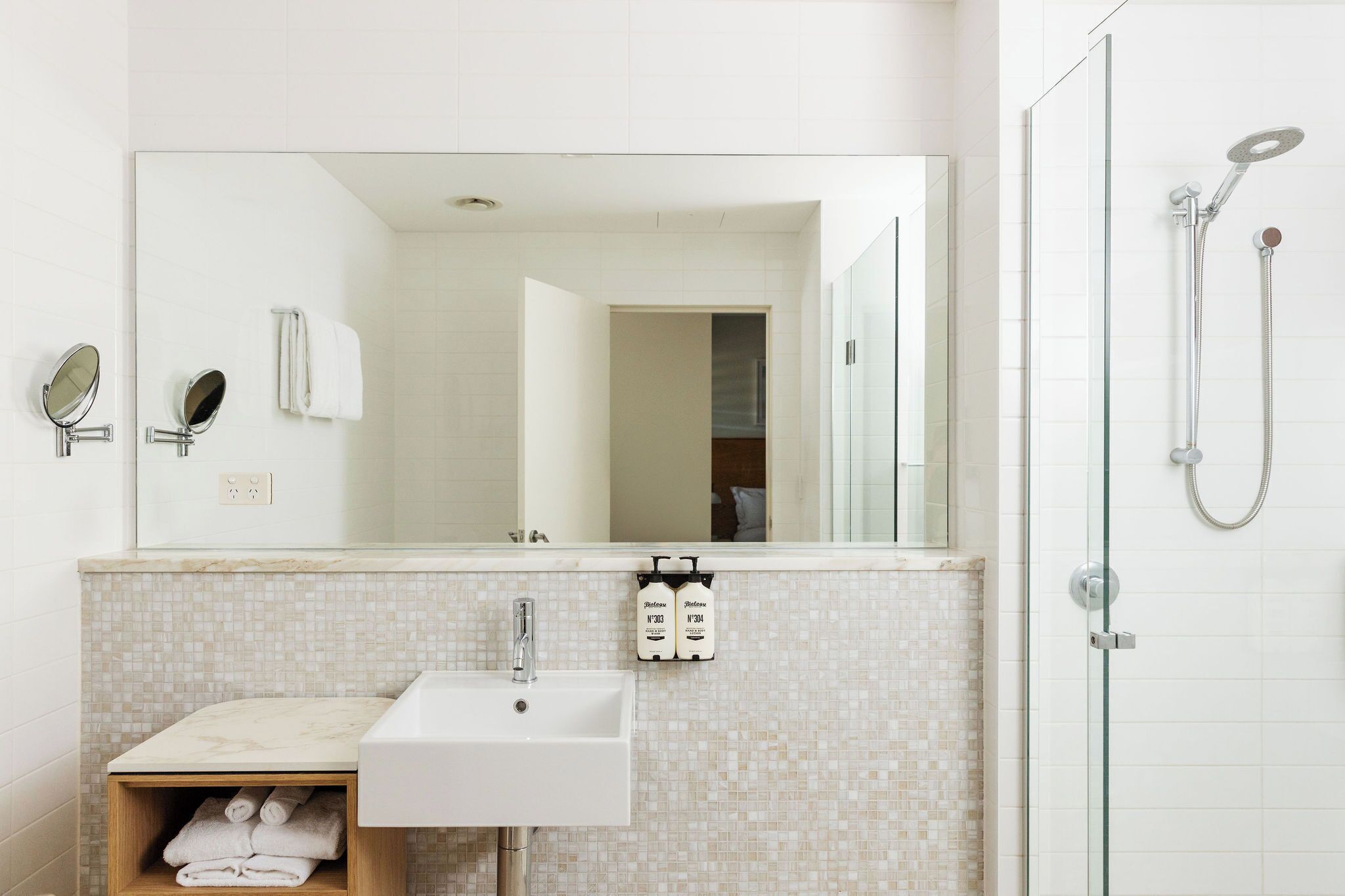 A bathroom with a sink, mirror, towel rack, and shower.