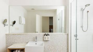 Un baño con lavamanos, espejo, toallero y ducha.